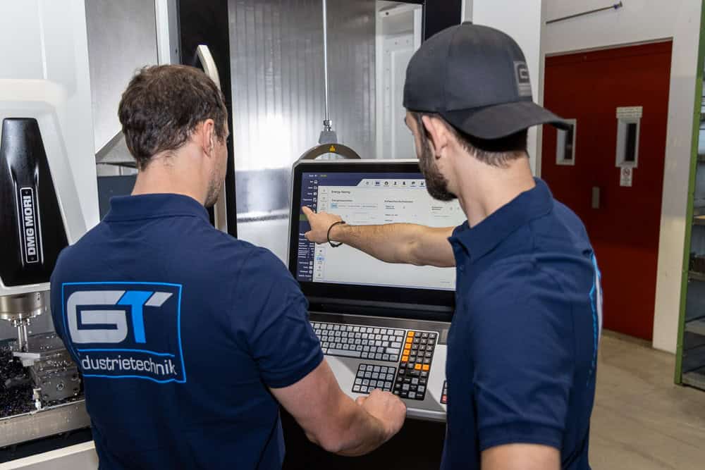 Zwei Männer in blauen Hemden arbeiten an einer CNC Maschine. Zwei Männer in blauen Hemden arbeiten an einer CNC Maschine.